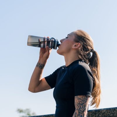 Fitness young sportswoman girl with tattoos doing sports in the morning drinking water while exercising outdoors in the city in park health